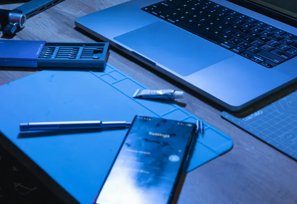 Laptop, Notizbuch und technische Arbeitsmittel auf einem Schreibtisch.